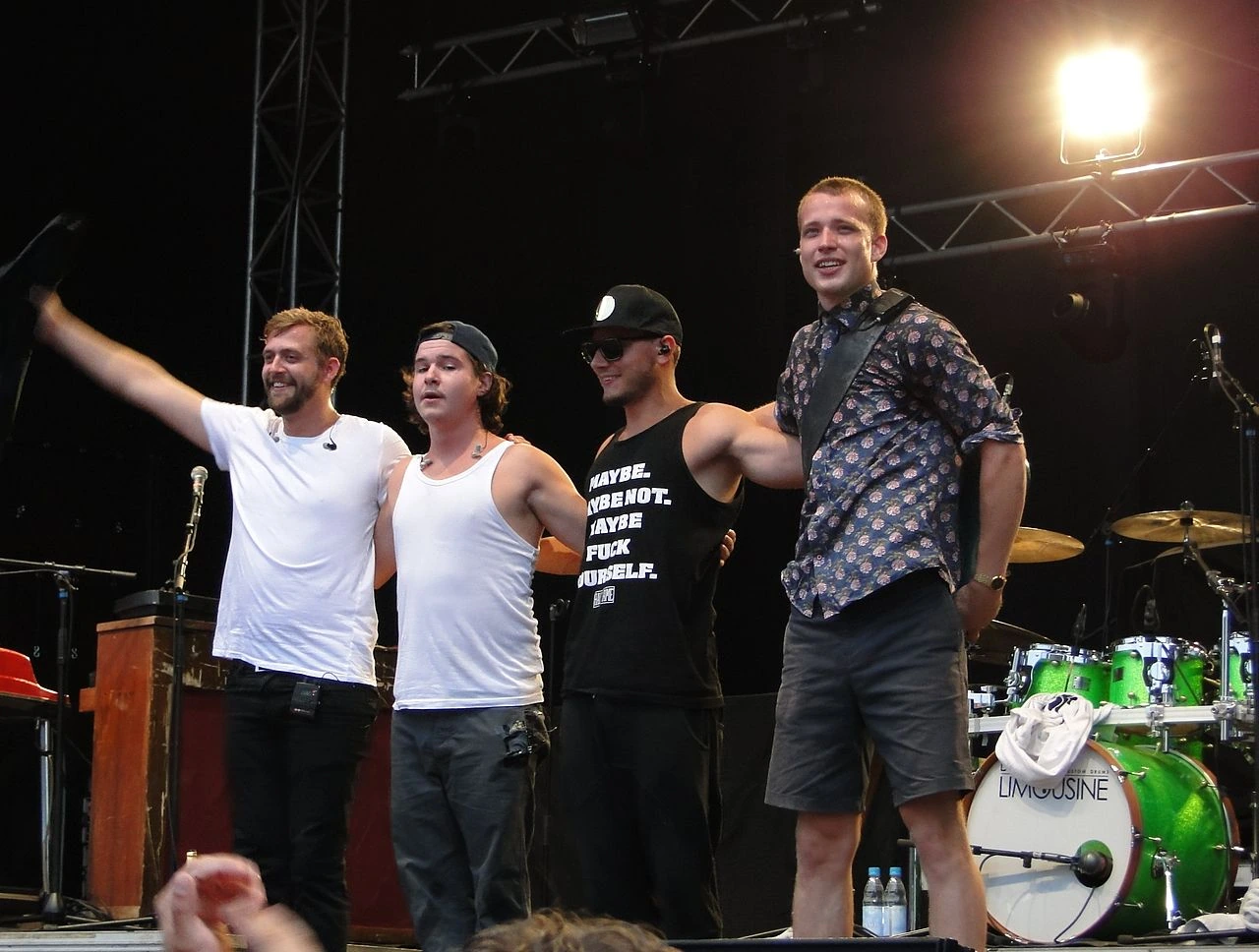 Lukas Graham performing on stage at a concert, with band members standing in front of the drum kit