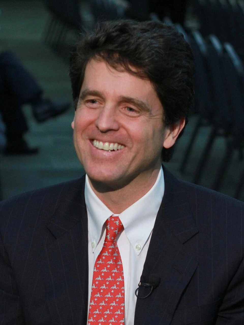 Mark Shriver smiling in a formal suit and red tie
