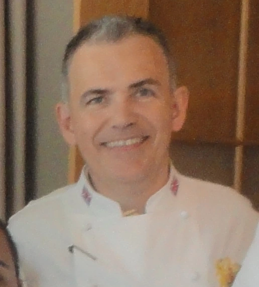 Portrait photo of chef Mark Flanagan in a white chef coat, smiling indoors.